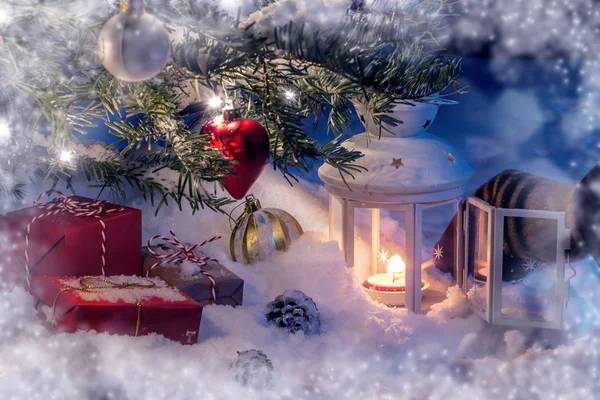 Рождественская композиция - ёлка в снегу, подарки, украшения и рука, освещающая фонарь спичкой — стоковое фото