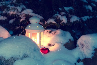 Kar yığınları evin avlusunda karla kaplı bir Noel ağacının altında yanan bir mum ile Fener