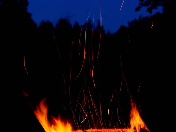 Flamme de feu de camp avec de longues étincelles sur le fond de la forêt nocturne — Photo