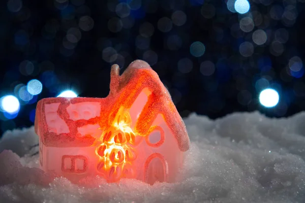 Glowing toy house in the snow on the background of Christmas lights. Festive, Christmas or New Year concept