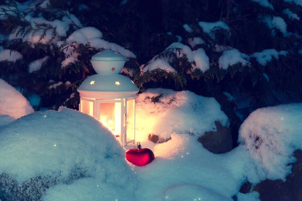 Lanterne avec une bougie allumée sous un sapin de Noël couvert de neige dans la cour de la maison dans les neiges — Photo