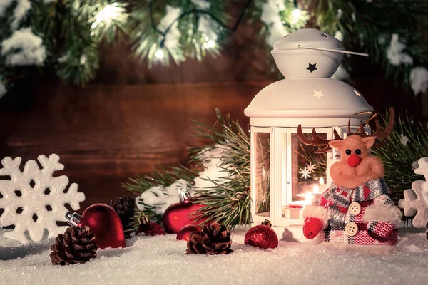 Lanterna branca com uma vela acesa fica na neve cercada por decorações de Natal no fundo de uma parede de madeira, galhos de árvore de Natal e luzes — Fotografia de Stock