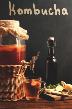 Taze ev yapımı Kombucha manyetasyonlu çay içeceği kavanozda musluk ve siyah arka plan, dikey görüntü üzerinde fincan ve şişe