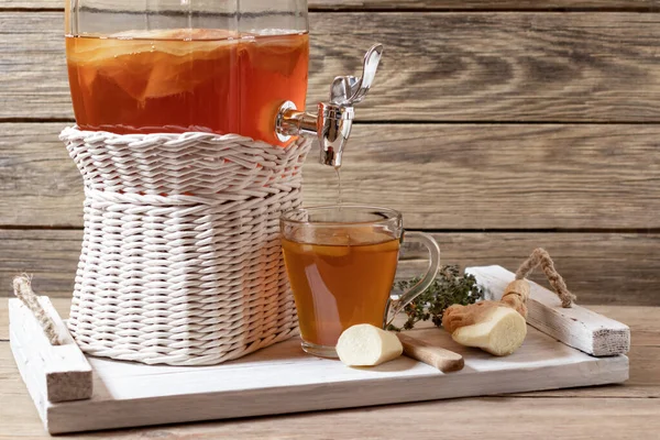 Fresh homemade kombucha fermented tea drink in a jar with faucet and in a cup on a white tray on a wooden background, copyspace
