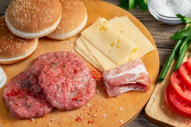 Ev yapımı hamburgerlerin, köftelerin, domateslerin, peynirin ve diğer malzemelerin ahşap bir arka planda pişirilme süreci.