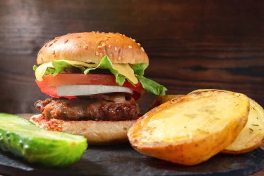 Taze ev yapımı burger ve ahşap arka planda salatalıklı fırında patates.