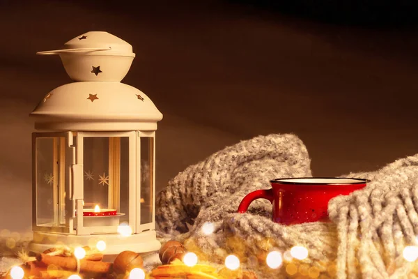 Lantaarn met een brandende kaars, specerijen en een rode mok met warme koffie op een besneeuwde houten tafel — Stockfoto