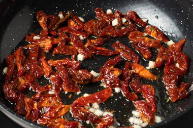 Makarna sosu yapmak için sarımsaklı ve biberiyeli tavada kurutulmuş domates. İtalyan mutfağının aşamaları