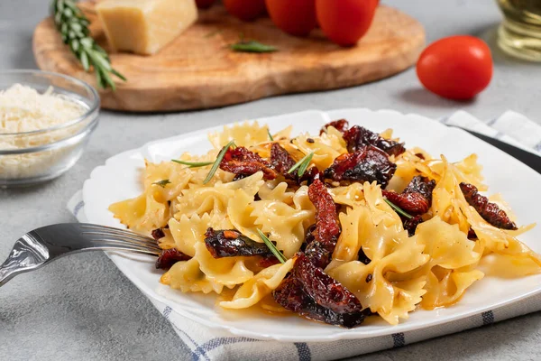 Pasta con tomates secados al sol y parmesano en un plato blanco sobre la mesa. Cocina italiana, ingredientes y el plato terminado — Foto de Stock