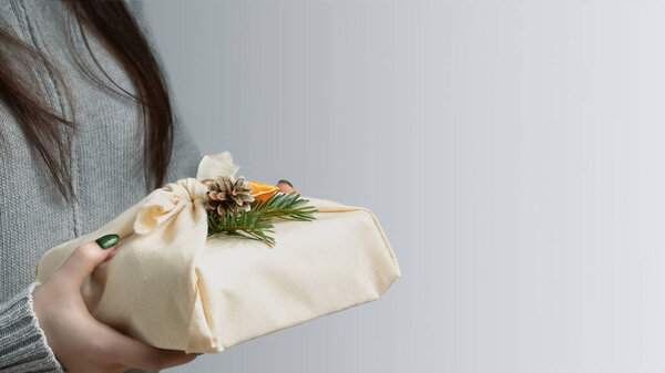 Отходы и экологически чистые технологии. Молодая женщина держит в руках подарок, завернутый в натуральную ткань и украшенный натуральными материалами
