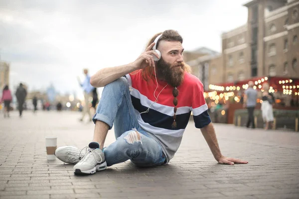 Guy with long beard and long hair, sitting in the street, listening music