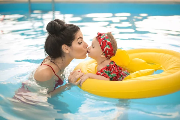 Lovely mom kissing her baby while swimming in the swimming pool