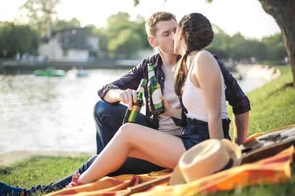 Sweet couple drinking beer at the park, in front of the lake