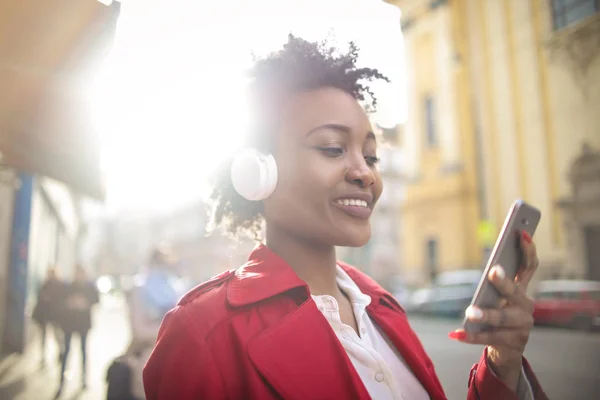 年轻女子一边用耳机听音乐 一边检查她的智能手机 — 图库照片
