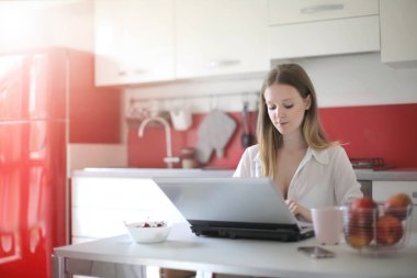 Genç ve güzel bir kadın mutfakta dizüstü bilgisayar kullanıyor. 