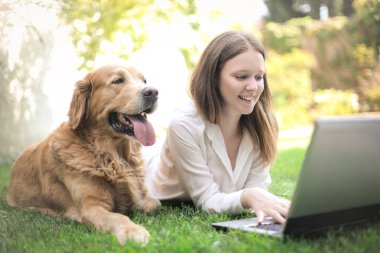 Genç ve güzel bir kadın dışarıda sevimli köpeğiyle dizüstü bilgisayar kullanıyor.