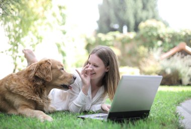 Genç ve güzel bir kadın dışarıda sevimli köpeğiyle dizüstü bilgisayar kullanıyor.