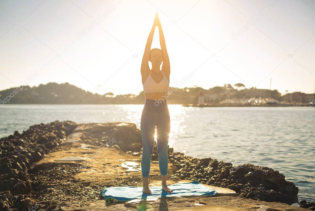 Girl doing yoga on a rock at the sunrise