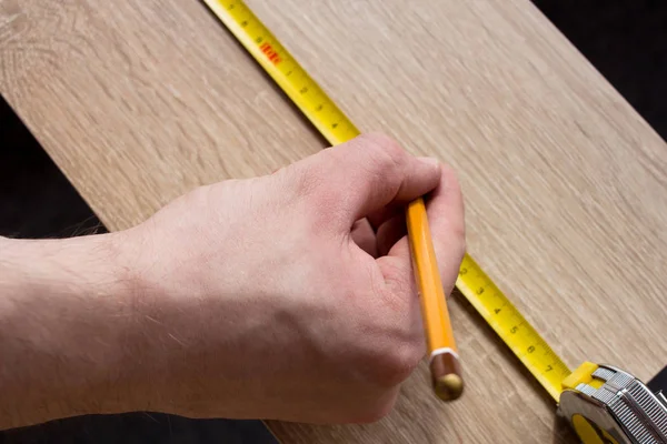 Manos de hombre midiendo tablón de madera con una línea de cinta . — Foto de Stock