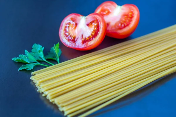 Uncooked pasta with tomatoes on a dark background.