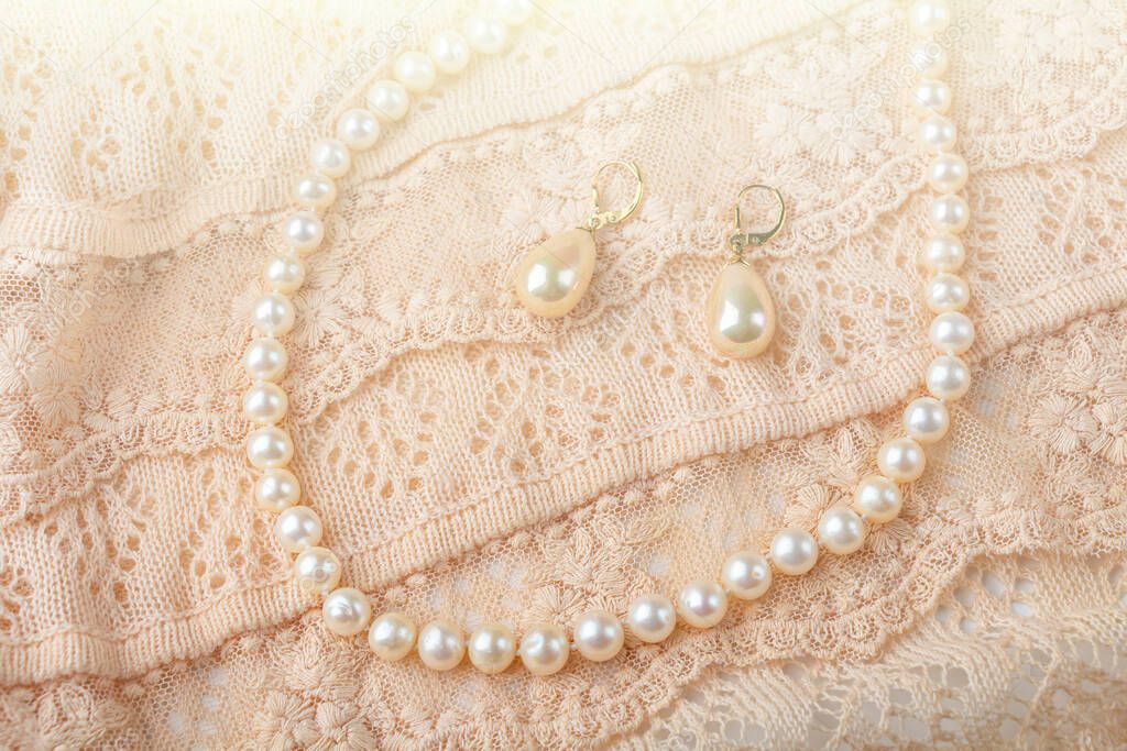Wedding background. Vintage pearl jewelry earrings and necklace on delicate ivory-colored lace cloth. Elegant gift for woman. Backlight