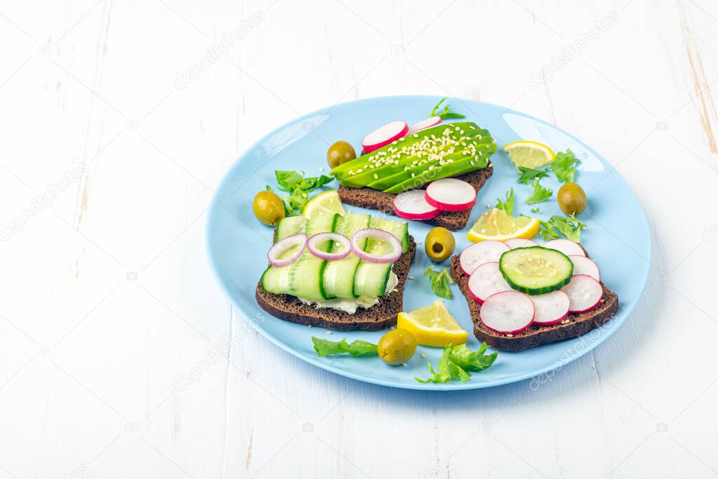 Superfood open vegetarian sandwich with different toppings: avocado, cucumber, radish on blue plate on white background. Healthy eating. Organic and veggie food. Close up, copy space for text