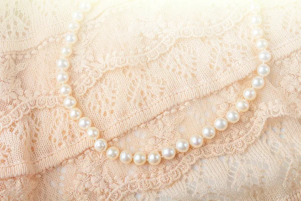 Wedding background. Vintage pearl jewelry necklace on delicate ivory-colored lace cloth. Elegant gift for woman. Backlight
