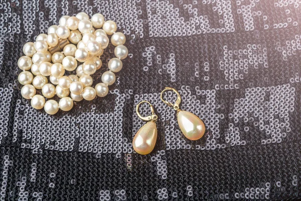 Vintage pearl jewelry on little black dress. Gatsby or Chicago fashion look. Luxury white necklace and earrings. Getting ready for party. Elegant gift for woman. Backlight