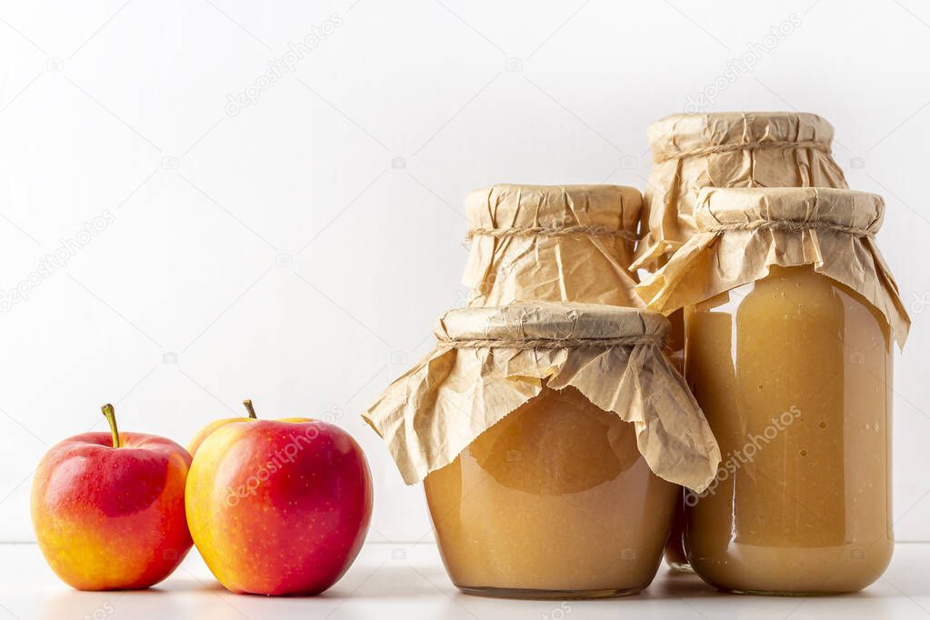 Canned and preserved applesauce in glass jars on white table. Fresh homemade fruit puree. Concept of proper nutrition and healthy eating. Organic and vegetarian food. Baby food