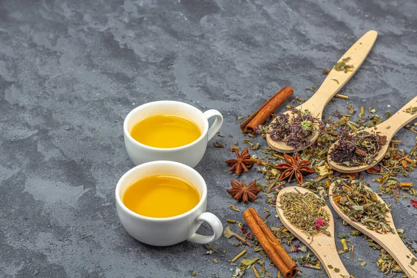 Assortment of different grade dry tealeaf in wooden spoons and two cup of green tea. Organic herbal, green and black tea with dry flower petals for the tea ceremony. Close up, copy space for text