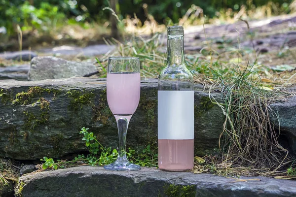 Opened bottle and wineglass with rose wine on rock. Mock up, copy space for text. Scenic still life with alcoholic drink in nature.