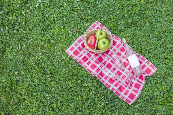 Romantic autumn picnic lunch outdoors. Wicker basket with baguette,   bottle of rose wine and apples on checkered cloth on stones. opy space for text