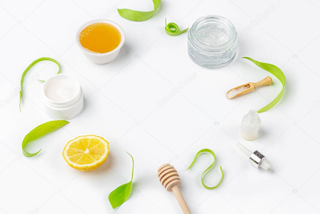 Natural organic ingredients to make home skin care. Cleansing and nourishing cosmetics. Beauty products: cream, honey, sea salt among green leaves on white background. Close up, copy space for text 
