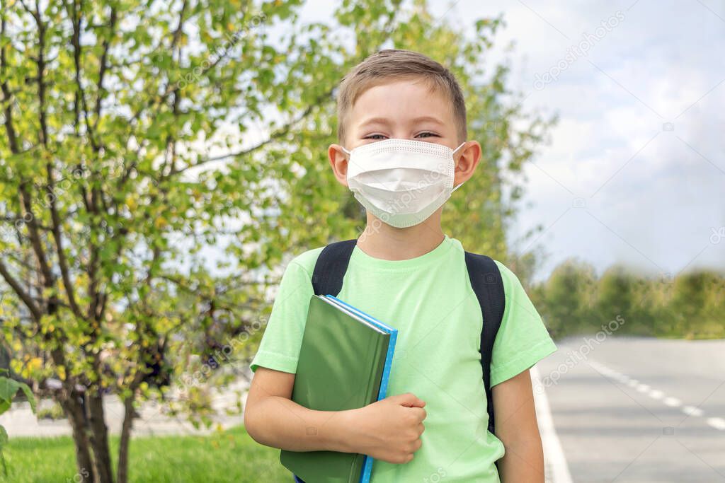 New normal, back to school. Schoolboy wearing medical mask and backpack holding textbook outdoors. Coronavirus protection. Keep your distanc