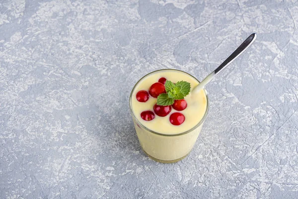 glass of yellow mango or banana yogurt or smoothie on gray background served with berries and mint. Healthy dairy drink. Vegetarian food. Copy space for text