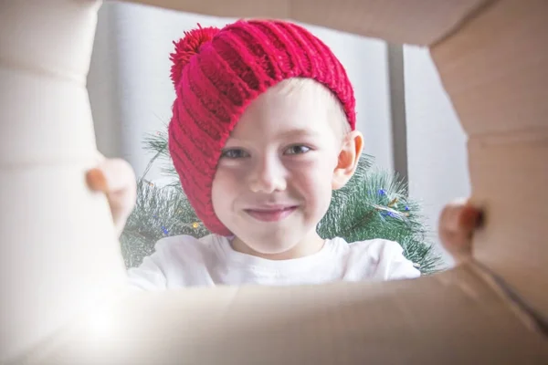 Мальчик Лет Красной Шляпе Открывает Коробку Подарками Смотрит Внутрь Удивлением — стоковое фото