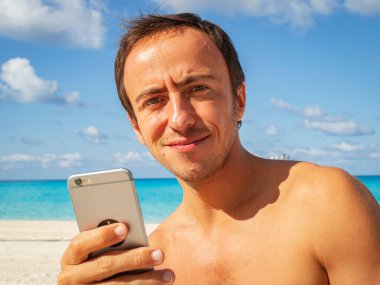 Plajda cep telefonu olan genç bir adam.