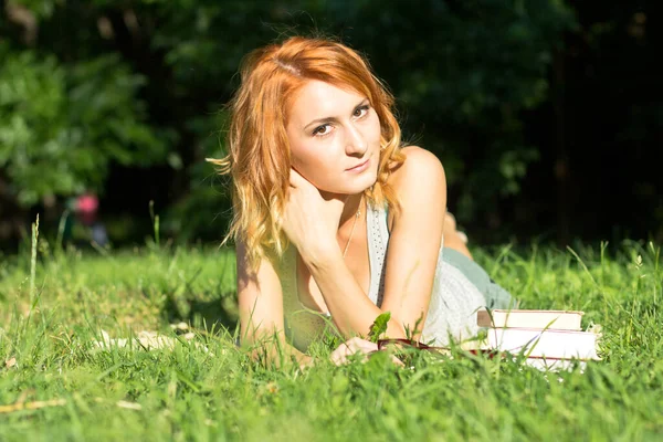 一个年轻的女孩正在户外看书 红头发的女人躺在草地上 — 图库照片