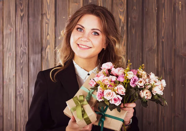 木の背景に花や贈り物を持つ若い笑顔の女性 — ストック写真