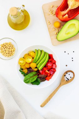 Beyaz masada taze sebze salatası. Dilimlenmiş domates, avokado ve biber yeşillikile. 