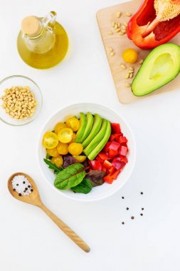 Beyaz masada taze sebze salatası. Dilimlenmiş domates, avokado ve biber yeşillikile. 