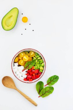 Beyaz masada taze sebze salatası. Dilimlenmiş domates, avokado ve biber yeşillikile. 