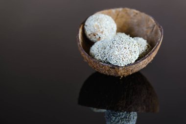 Karanlık bir arka plan üzerinde tarih meyve, fındık ve susam Enerji topları. Bir hindistan cevizi kabuğunda çiğ tatlı, bir kopya alanı ile.
