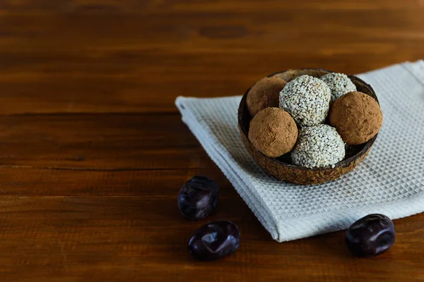 Energy balls of date fruits, nuts, cocoa and sesame on a wooden table. Raw dessert in a coconut shell, with a copy space.