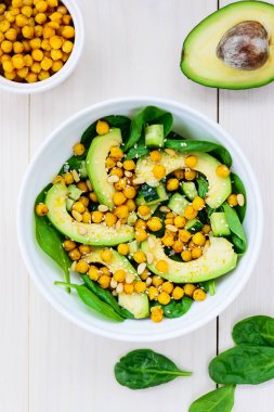 Beyaz ahşap masada avokado, nohut, ıspanak, salatalık ve susam dan salata.