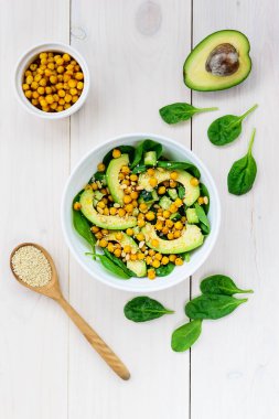 Beyaz ahşap masada avokado, nohut, ıspanak, salatalık ve susam dan salata.