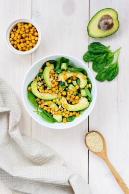 Beyaz ahşap masada avokado, nohut, ıspanak, salatalık ve susam dan salata.