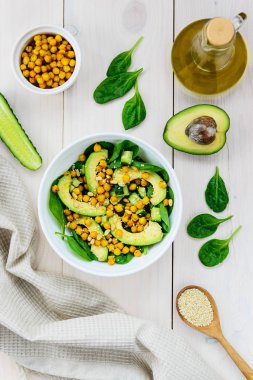Beyaz ahşap masada avokado, nohut, ıspanak, salatalık ve susam dan salata.