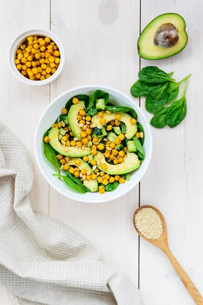 Beyaz ahşap masada avokado, nohut, ıspanak, salatalık ve susam dan salata.