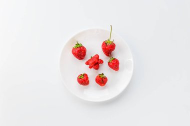 Beyaz tabakta çilek. Beyaz arka planda çirkin yemek, dikey yönelim, üst görünüm.